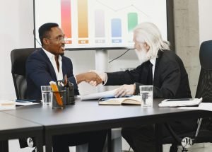 pexels-photo-6285094-6285094 Two diverse businessmen in suits shaking hands over a desk in a modern office.